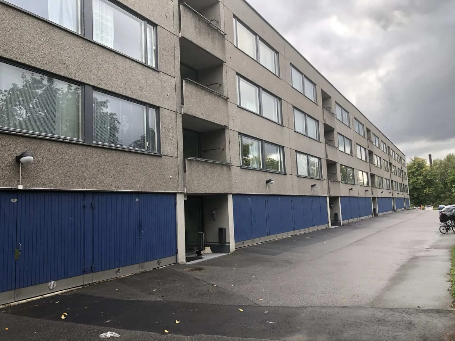 Harmaa kerrostalo, jossa on siniset autotallin ovet ja tumma taivas.