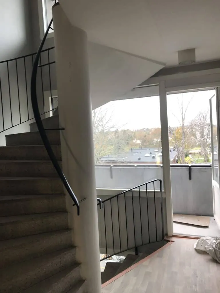 Sisätiloissa on kierreportaat, valkoinen pylväs ja musta kaide, sekä näkymä ulos parvekkeelle.