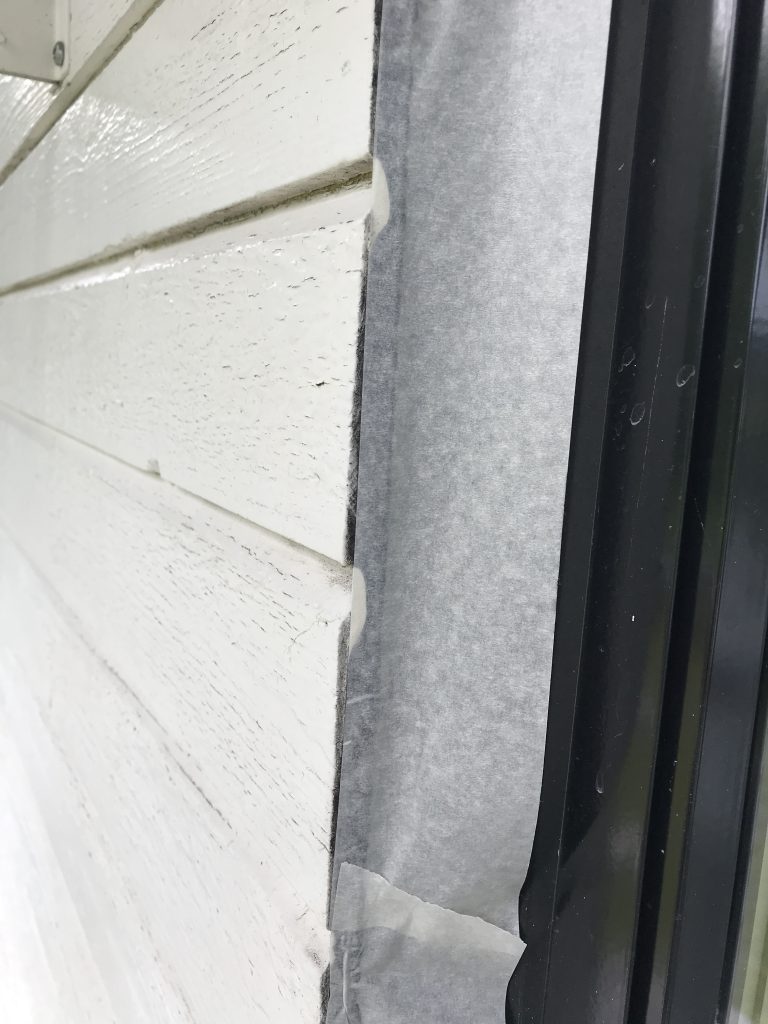 Lähikuva valkoisesta puupaneloinnista, jossa on maalarinteippi ja musta ikkunan kehys. Valo on kirkas ja tasainen.