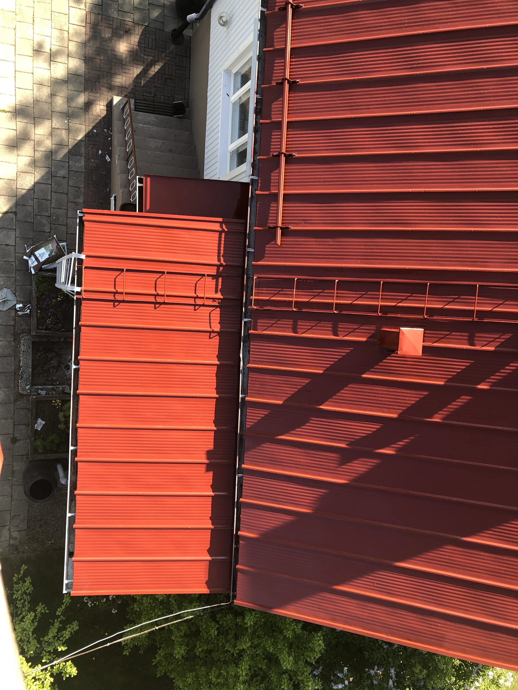 Ylhäältä otettu kuva punaisesta peltikatosta, jossa on varjoja ja kattotikkaita.