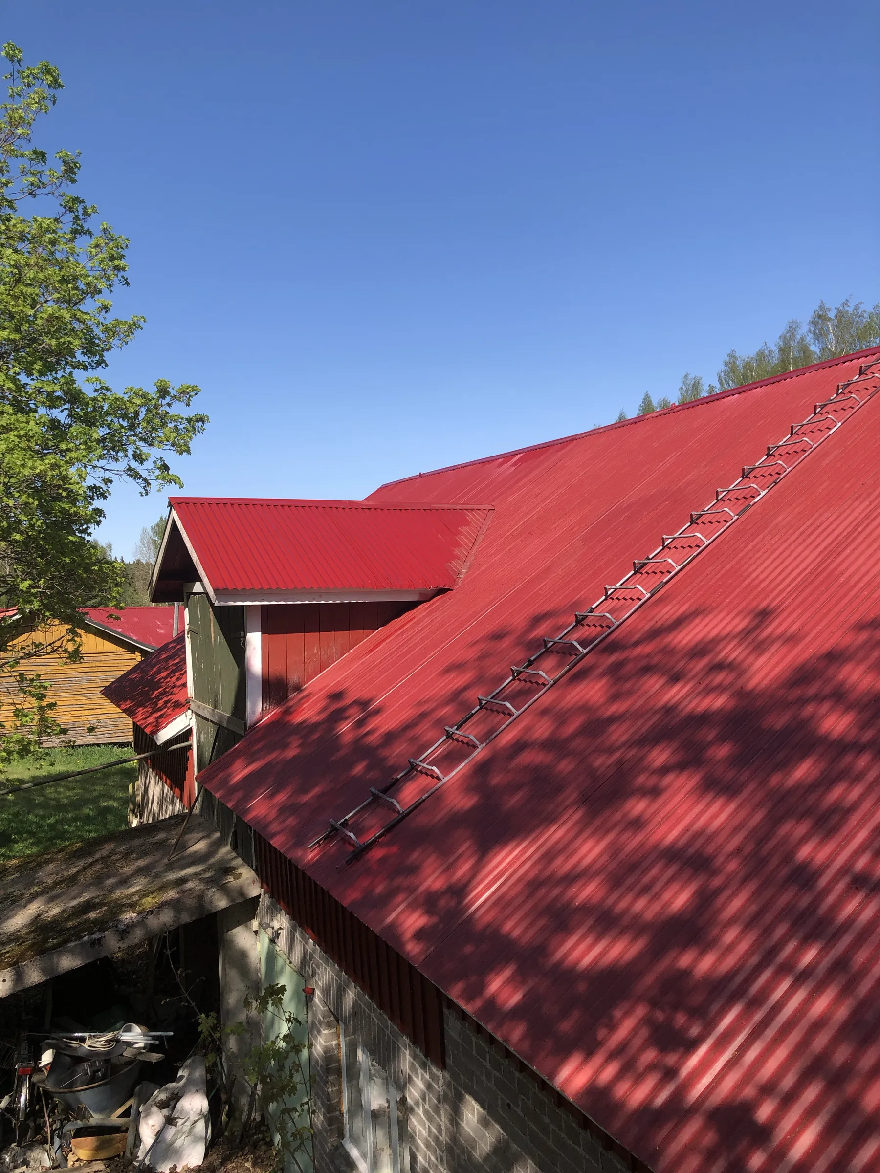 Punainen peltikatto, metallinen tikapuu, sininen taivas.