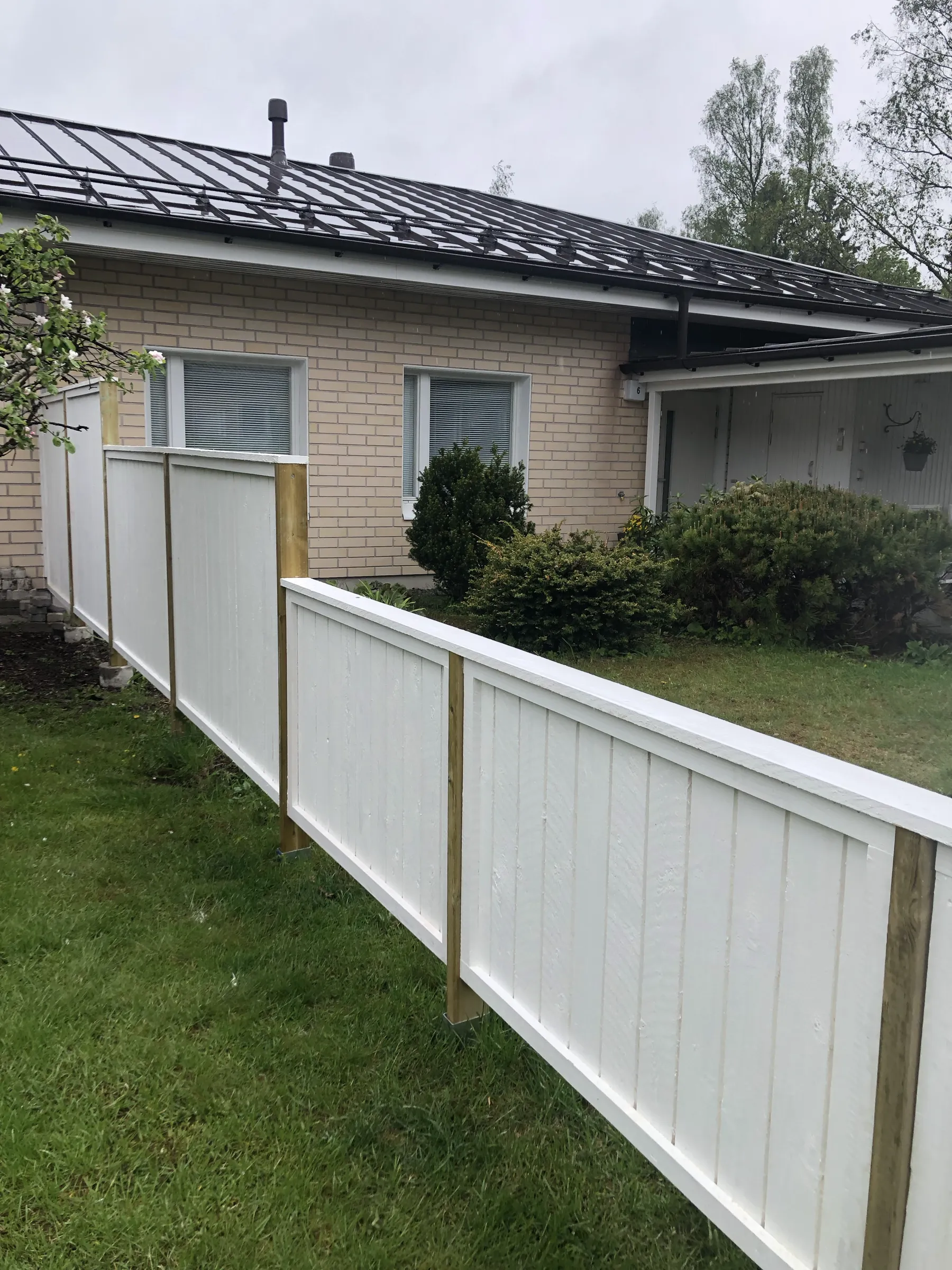 Valkoinen puuaita vihreällä nurmikolla, tiilitalo taustalla.