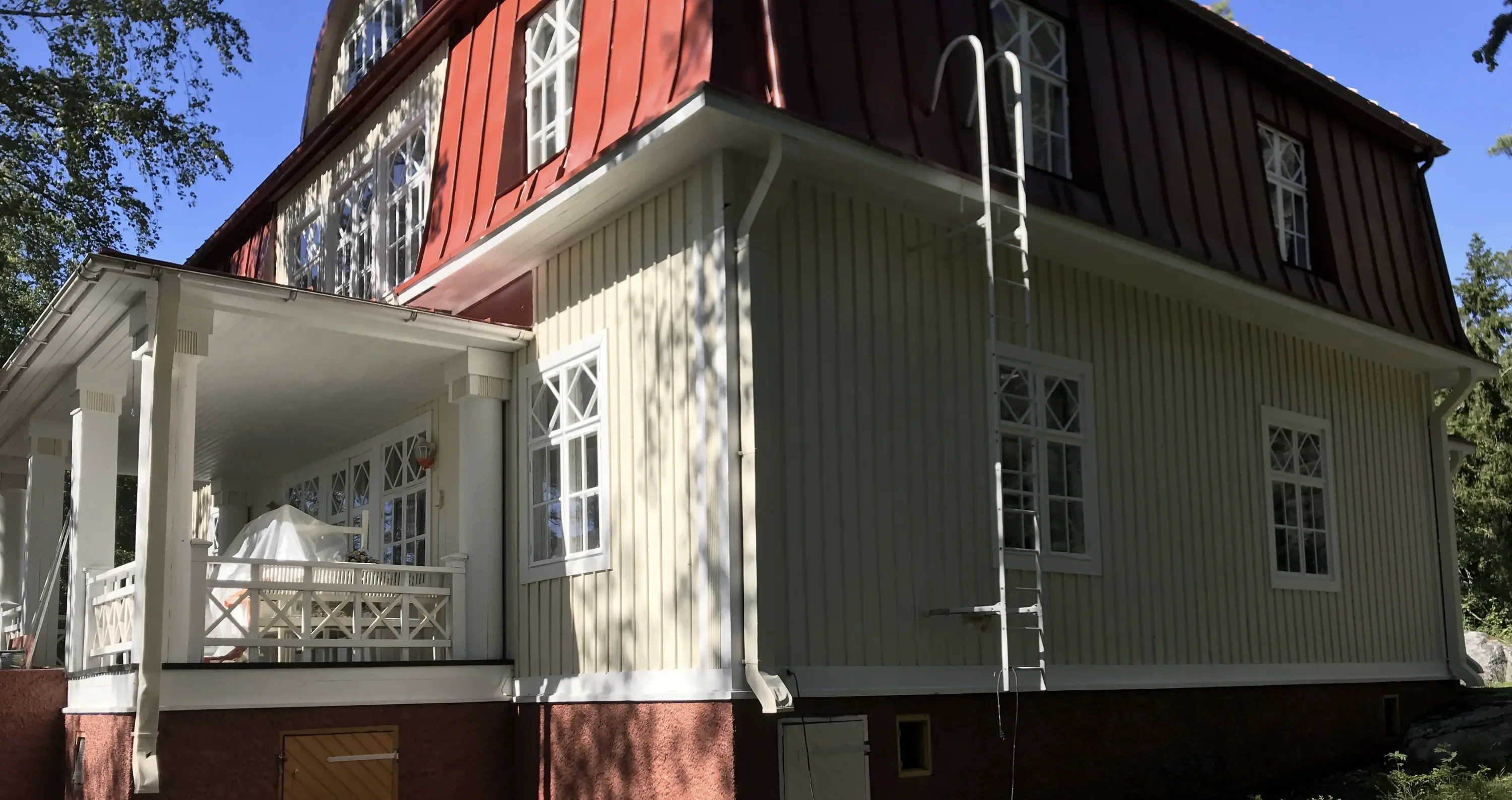 Vaaleankeltainen puutalo punaisella katolla, jossa on valkoiset ikkunat ja valkoinen kuisti.