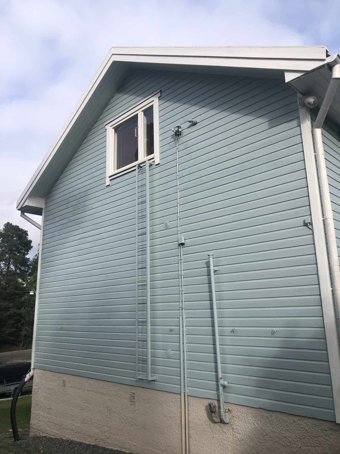 Vaaleansininen puutalo, jossa valkoiset ikkunankarmit, tikkaat ja sadevesiputket. Valoisa sää.