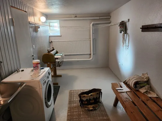 Pyykinpesuhuoneessa on pesukone, kuivausteline, penkki ja matto. Huone on valoisa ja siisti.