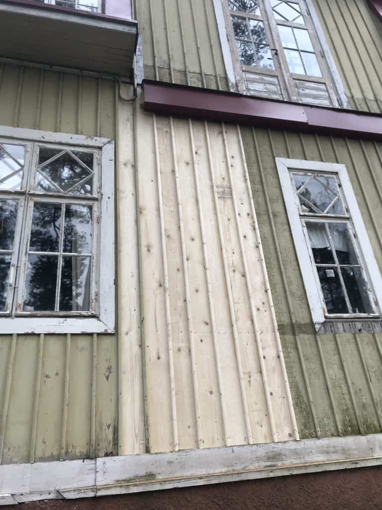 Ulkokuva vanhasta rakennuksesta, jossa on kaksi ikkunaa ja uusi puupanelointi, valaistus on luonnollinen.