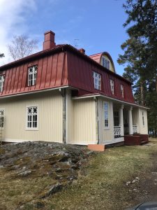 Vaaleankeltainen rakennus punaisella katolla, valkoiset ikkunat ja pylväät.