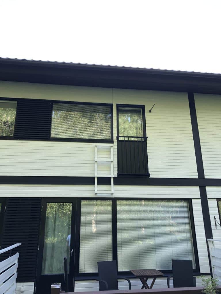 Kaksikerroksinen valkoinen talo, jossa on mustat ikkunakehykset ja valkoinen tikapuu yläkerran ikkunan vieressä.