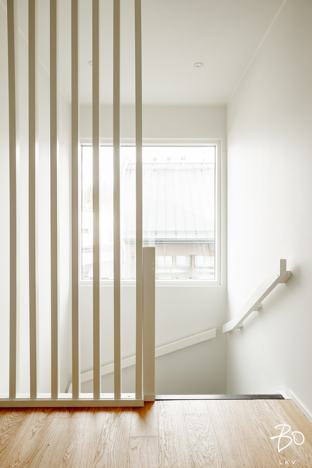 Vaaleassa sisätilassa on puinen lattia, valkoiset pystysuorat säleet, ikkuna ja portaat, joissa on valkoiset kaiteet.